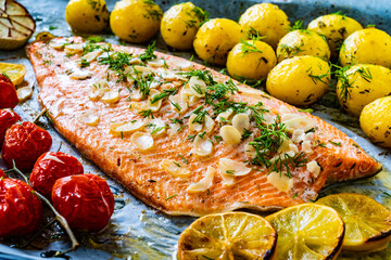 Wall Mural - One sheet pan Roast trout fillet with potatoes and vegetable salad served on black stone plate on wooden table
