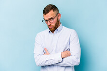 Young Caucasian Man Isolated On Blue Background Frowning Face In Displeasure, Keeps Arms Folded.