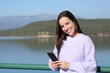 © PheelingsMedia - Happy woman holds phone and looks at camera in a lake