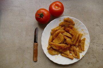 Patatas cocinadas al horno, dos tomates y un cuchillo para cortar. Colores amarillos y rojos. 