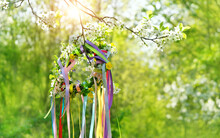 Spring Flower Wreath With Colorful Ribbons In Garden, Green Natural Background. Floral Decor. Symbol Of Beltane, Wiccan Celtic Holiday Beginning Of Summer. Pagan Witch Traditions And Rituals