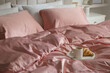 Croissant and coffee in breakfast tray on bed with beautiful pink silk linens indoors