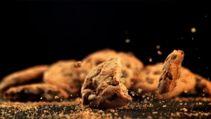 Canvas Print - cookies with pieces of chocolate fall on the table. on a black background. filmed is slow motion 100