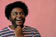 © Carlos David - young happy african american man hand on chin looking sideways at copy space posing in the studio over pink background