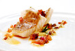 sea bass fillet with skin in olive oil and tomato and spices on a plate on a white background, close up view