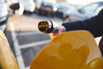 Wall Mural - Man holding electric car charger plug type 1 at charging station