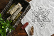 A top view image of a sacred geometry grid cloth and white sage smudge sticks in a brown wicker basket. 