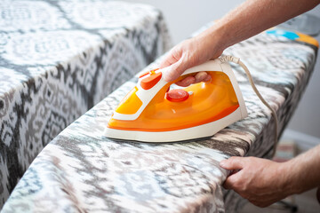 A man holds an iron in his hands, ironing the curtains on an ironing board. Household chores