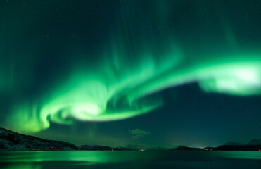 whirling aurora borealis in nightsky reflecting on sea and land