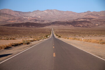 Looking down the middle of a long straight desert road with no one in site for miles in the Death Valley
