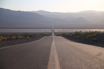 Desert road with yellow lane stretching straight through desert Death Valley