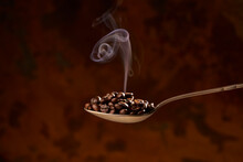 Spoon Full Of Heated Coffee Beans On Brown Background