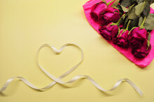 Bouquet Of Red Roses Lies On Yellow Background. Heart Made From White Ribbon.