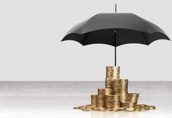 Wall Mural - Holding a small umbrella over a pile of coins on the table. Financial safety and investment concept.