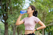 © PBXStudio - Portrait of a beautiful Asian woman drinking water from a bottle to refresh her body after she runs a workout. She is listening to music through bluetooth headphones. Concept of woman runners.