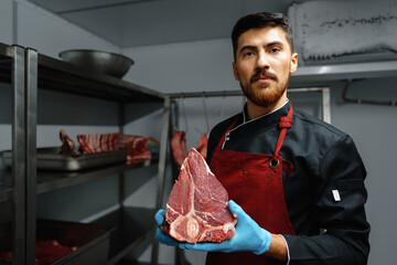 Wall Mural - Young butcher holding raw meat steaks in fridge of grocery shop