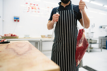 Wall Mural - Butcher man holding meat on hook to cut and sell it