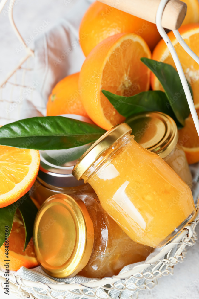 Basket with tasty orange jam in jars and leaves on table, closeup