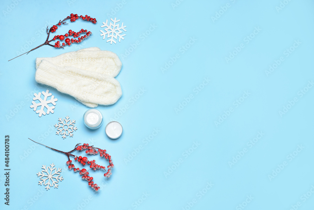 Composition with knitted mittens, jars with cream and winter decor on color background