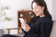 © lielos - 自宅リビングのソファーに座りスマホを見ているアジア人女性
