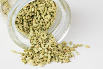 Scattered green dry fennel seeds on white background. fennel is ingredient of traditional Indian cuisine in condiments container, macro photo, selective focus