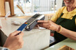 © DragonImages - Closeup image of smiling cafe worker accepting payment and giving card reader