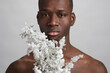 Serious young shirtless man with blooming branch looking at you while standing in front of camera on white background