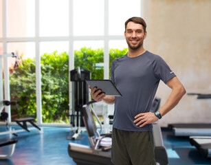 fitness, sport and healthy lifestyle concept - smiling man in sports clothes holding tablet pc computer over gym background