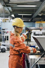 Young Female Industrial Worker In Uniform Using Manufacturing Machinery At Factory