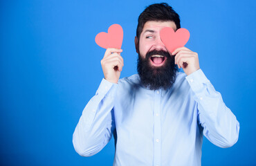 Love is the answer. Sexy valentine man covering eye with heart shaped decorations. Bearded man holding red hearts. Hipster with small hearts. Happy valentines day. The holiday of love and romance