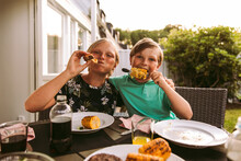 Portrait Of Siblings Eating Grilled Corn And Meat While Sitting In Back Yard