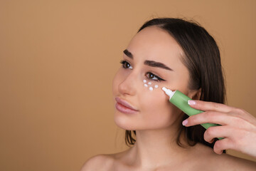 Wall Mural - Close beauty portrait of a topless woman with perfect skin and natural make-up, holding a cream for moisturizing and elasticity of the skin under the eyes