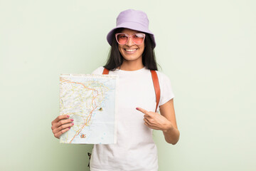 Wall Mural - young pretty hispanic woman smiling cheerfully, feeling happy and pointing to the side tourist and map concept