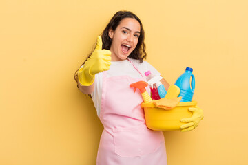 young pretty hispanic woman feeling proud,smiling positively with thumbs up. housework an clean products concept