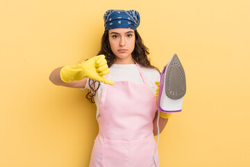 Wall Mural - young pretty hispanic woman feeling cross,showing thumbs down. iron and clothes concept