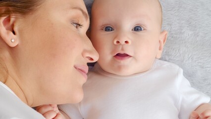 Wall Mural - Happy newborn baby with his mother. Healthy newborn baby in a white t-shirt with mom. Closeup Faces of the mother and infant baby. Cute Infant boy and parent, top view. Happy family portrait