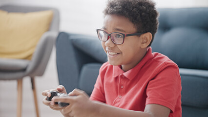 Wall Mural - Active boy playing video game with console sitting on floor in room, having rest