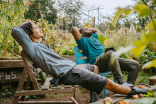 Male Farmers Resting On Wooden Chair In Urban Garden