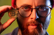 © khosrork - Closeup portrait of serious hipster guy in glasses showing golden coin bitcoin crypto currency, electronic virtual money. Indoor studio shot isolated on colorful neon light background.