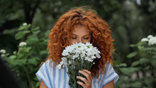 Curly Redhead Woman With Closed Eyes Smelling White Flowers.