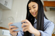 © hurricanehank - Happy asian girl playing mobile game on mobile phone. Excited young Vietnamese woman plays video games on modern smartphone gadget. Cute southeast asian female enjoy gaming online