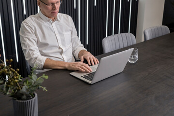 Poster - Concentrated and serious mature businessman sitting at conference table. Man looking at laptop screen and analyzing information or preparing for corporate discussion or meeting. High quality photo
