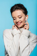 © LIGHTFIELD STUDIOS - Smiling woman in sweater using earphone isolated on blue.