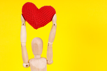 Canvas Print - wooden man with a red heart in his hands on a yellow background