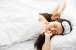 © Aleksandr Rybalko - Happy awakening of a young woman from a dream. A woman in bed wearing a sleep mask stretches, looks at the camera and smiles. The concept of good morning.