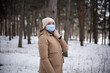© Javvani - A young woman in winter clothes and a medical mask walks in the winter forest.