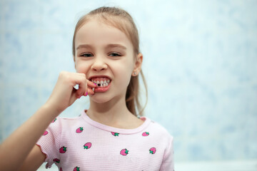 Girl child shows her mouth without one missing milk tooth. The girl holds a fallen milk tooth in her hands. A child without a front milk tooth in his bathroom. Preschool dental care