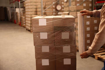 Wall Mural - Worker wrapping boxes in stretch film at warehouse, closeup