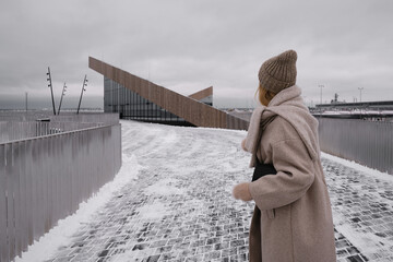 The girl stands on a modern bridge in the city in winter and looks into the distance. Tourist walks in Europe. Urban lifestyle