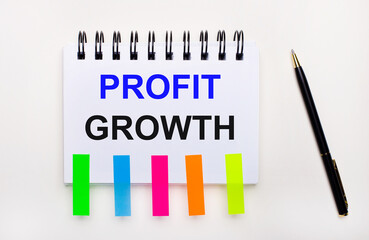 Fototapete - On a light background, a pen, a notebook with the text PROFIT GROWTH and bright stickers.